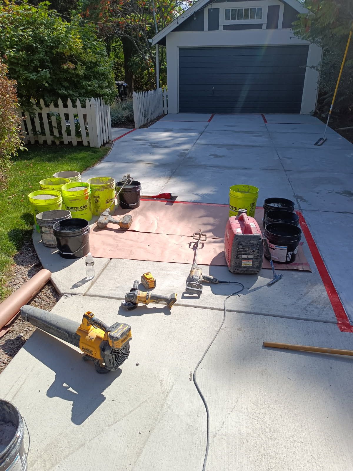 Driveway with painting supplies, buckets, tools, and a red-marked work area in front of a garage.