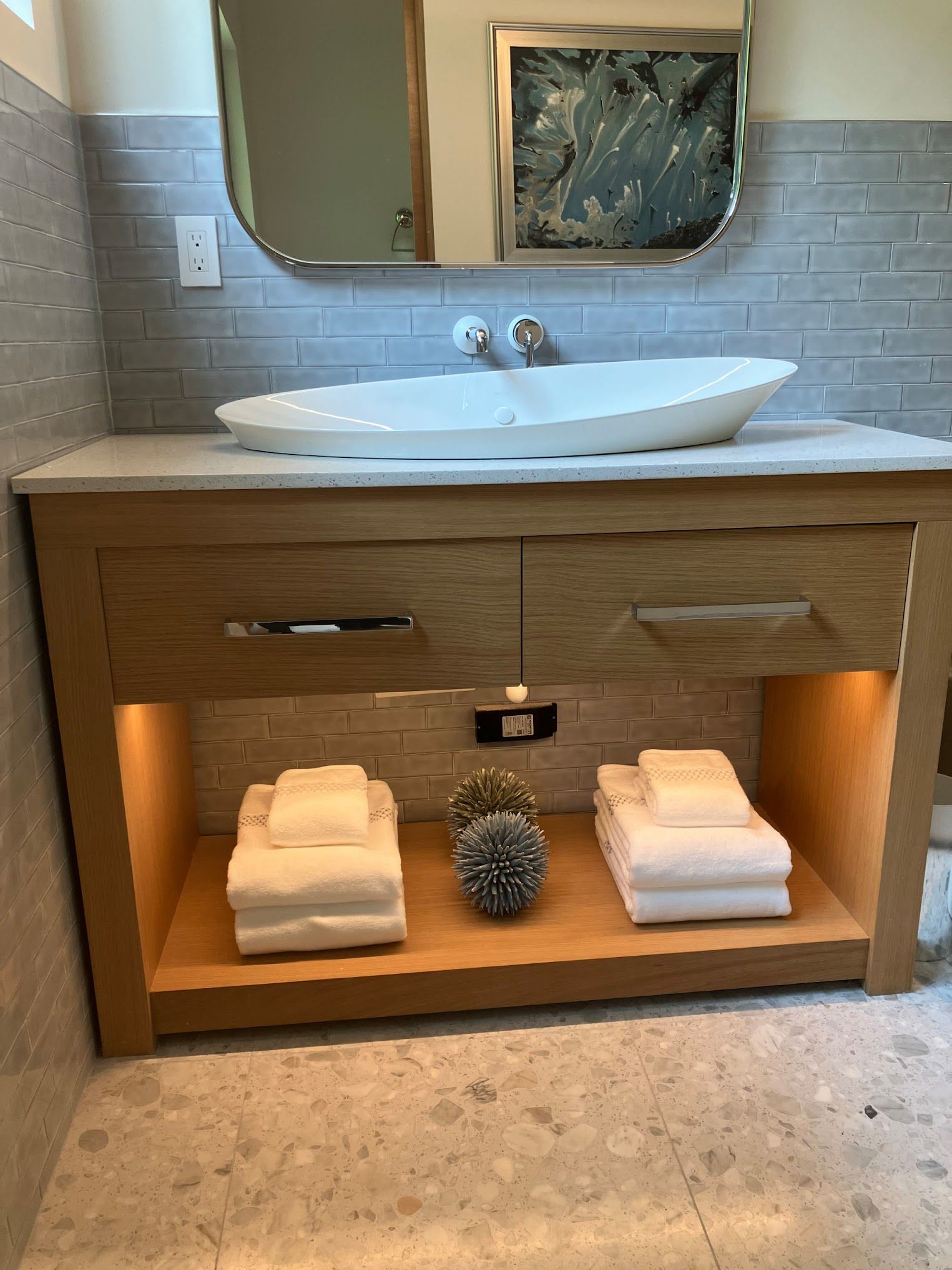 A bathroom with a sink , mirror and towels on a shelf.