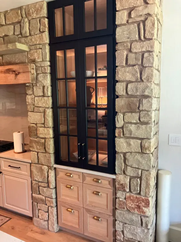 A kitchen with a stone wall and black cabinets