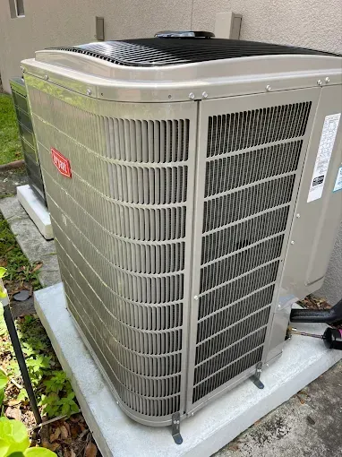 A beige Bryant central air conditioning unit sits on a concrete pad outdoors next to a building wall.
