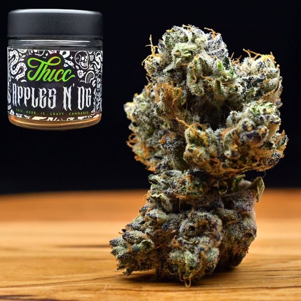 Cannabis bud beside a black jar labeled “Apple Fritter” on a wooden surface
