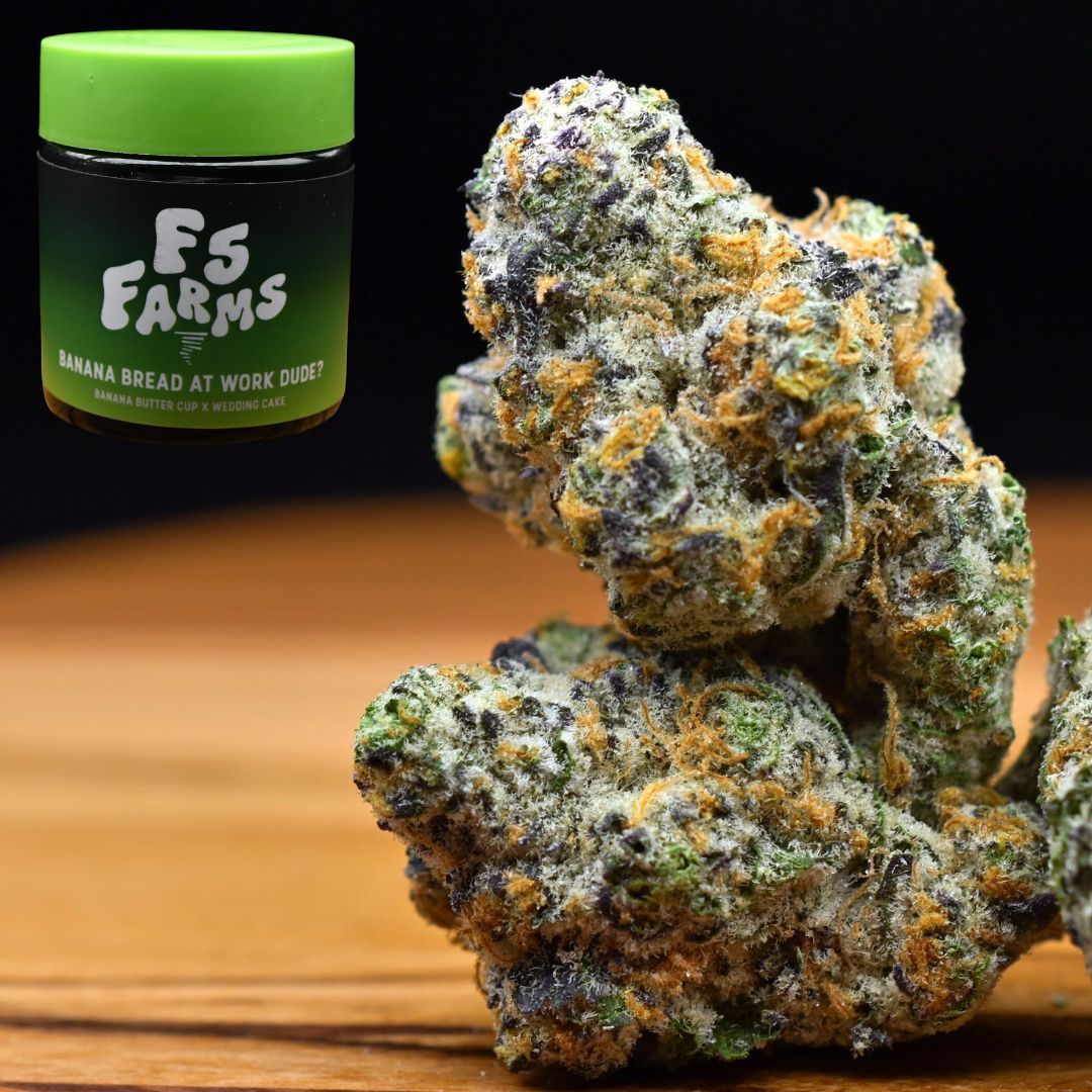Two frosty cannabis buds beside a green FS Farms jar on a wooden surface.