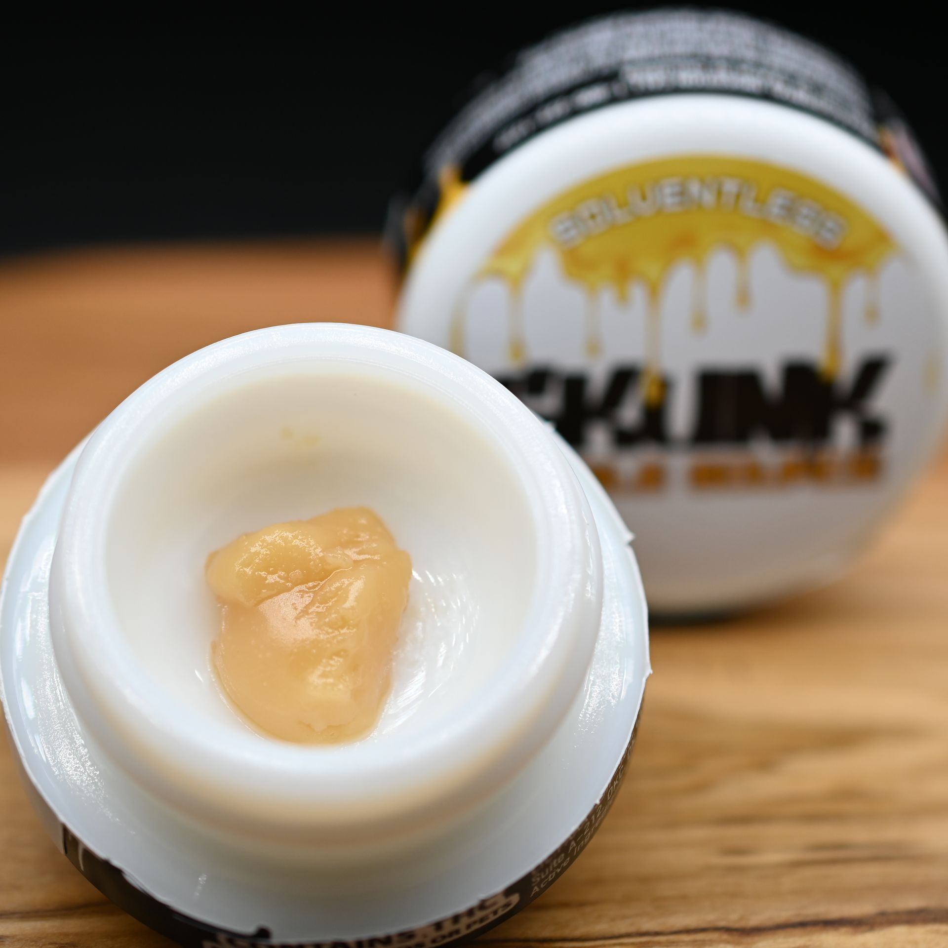 Open jar of beige balm on wood, with labeled container blurred in the background