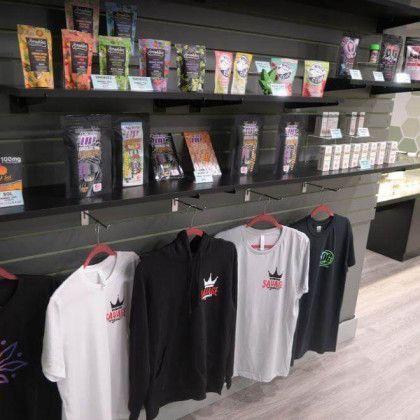 Black shelves displaying small colorful packages above hanging black and gray graphic T-shirts in a retail store