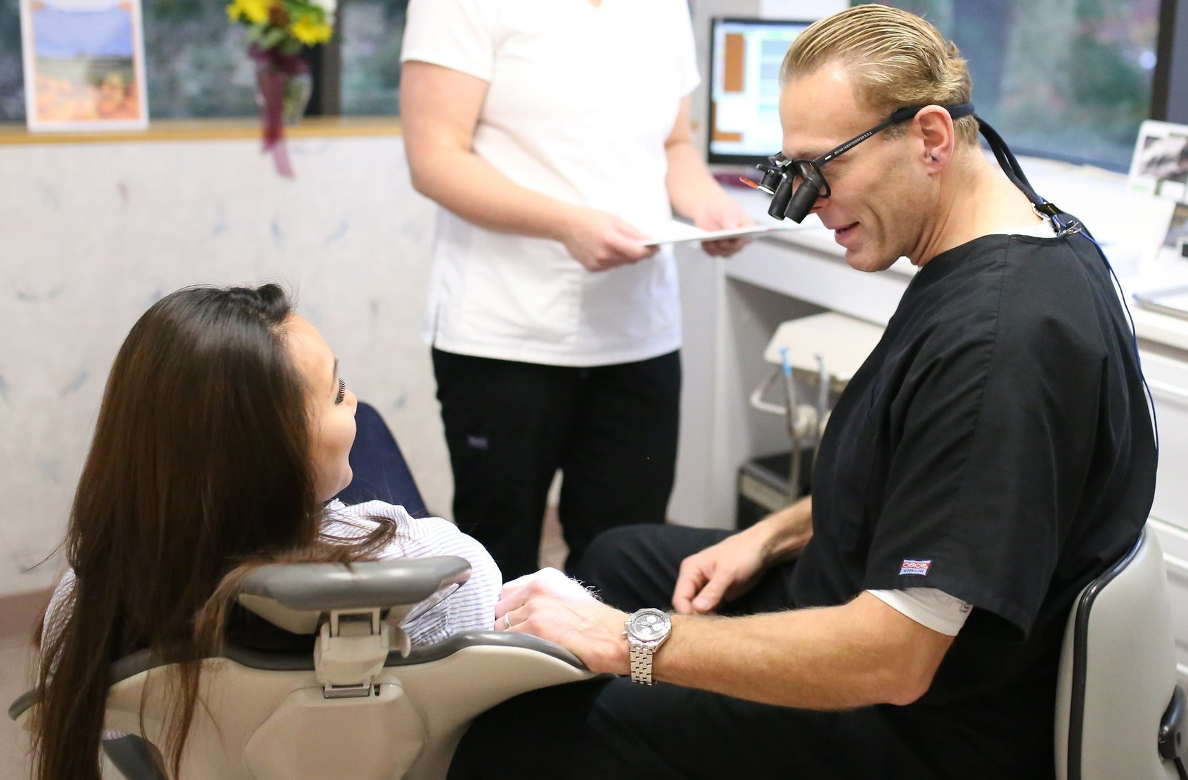 A woman is sitting in a dental chair talking to a dentist