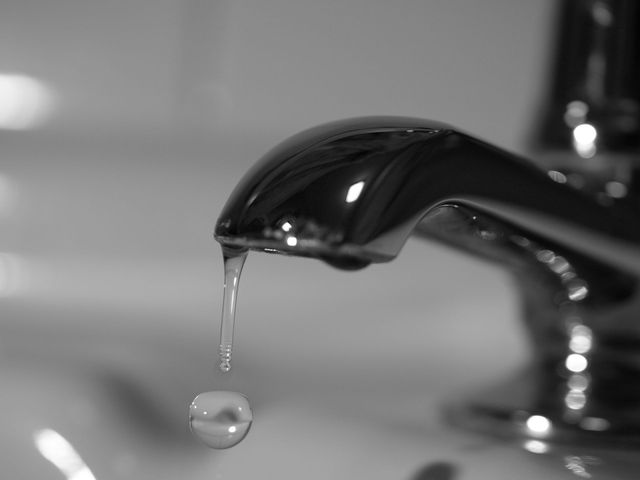 Black-and-white close-up of a faucet dripping water into a sink