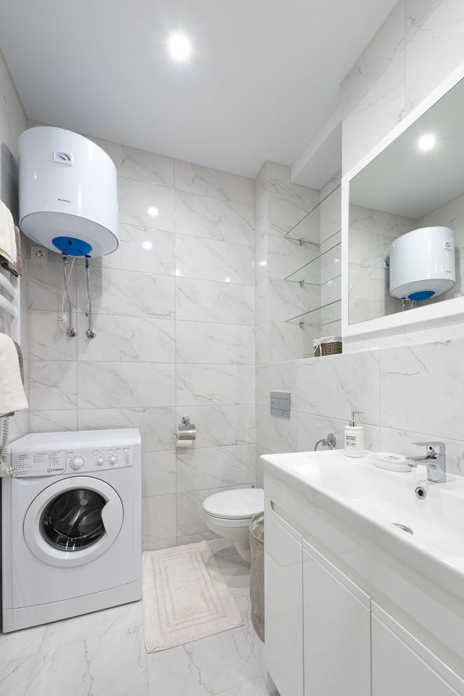 Compact white bathroom with a washing machine, sink, toilet, shower, and large mirror.