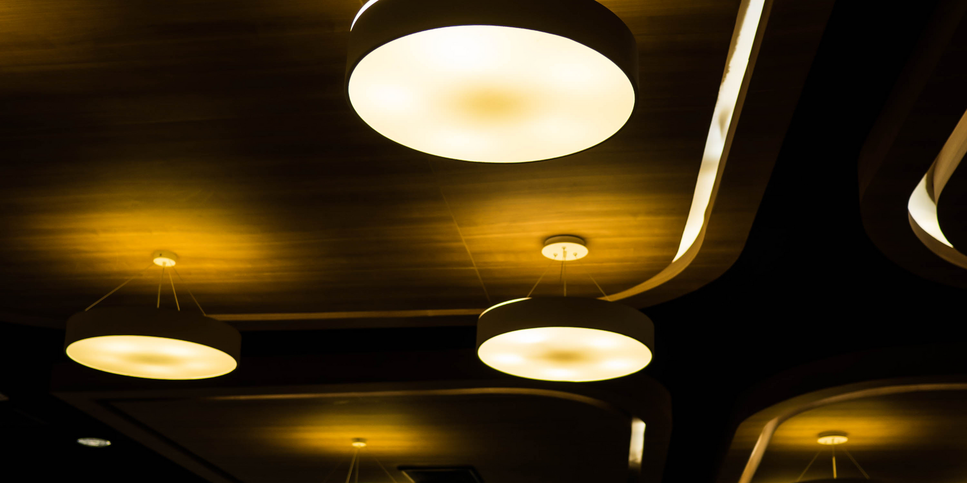 Low angle view of a ceiling with pendant lights. The lights have a warm, yellow glow against a dark background.