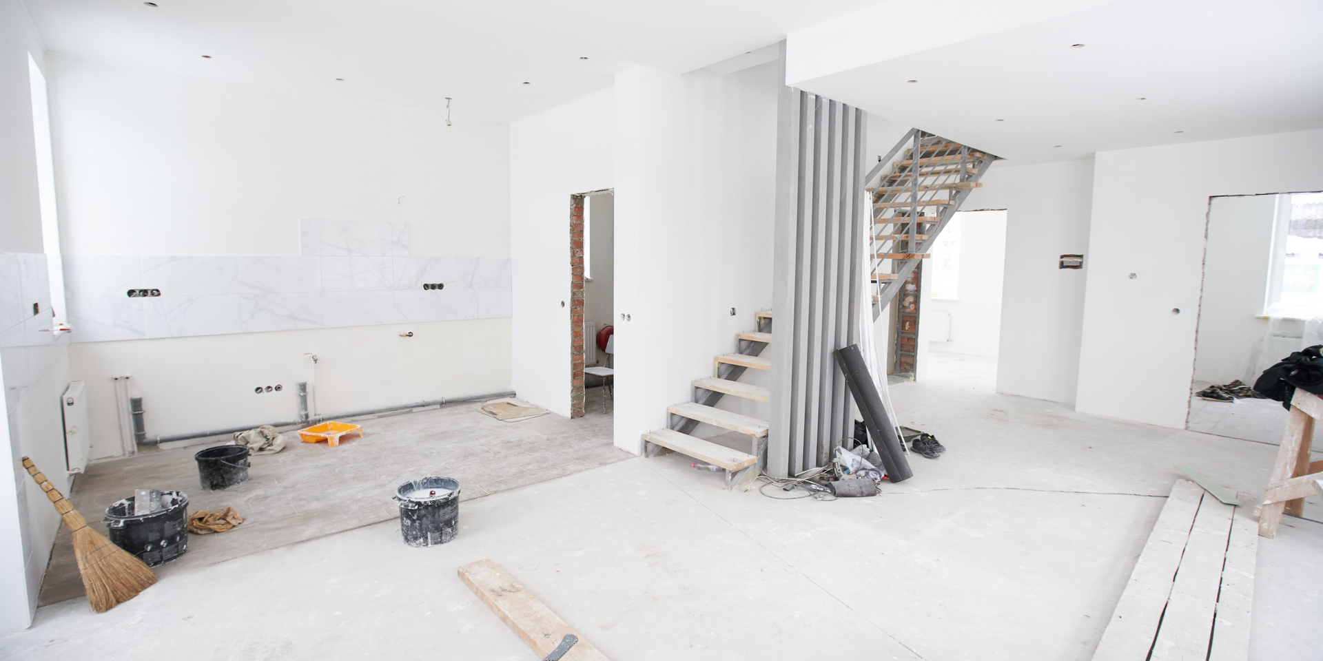 Interior under renovation, featuring exposed drywall, stairs, and construction materials. Bright, unfinished space.