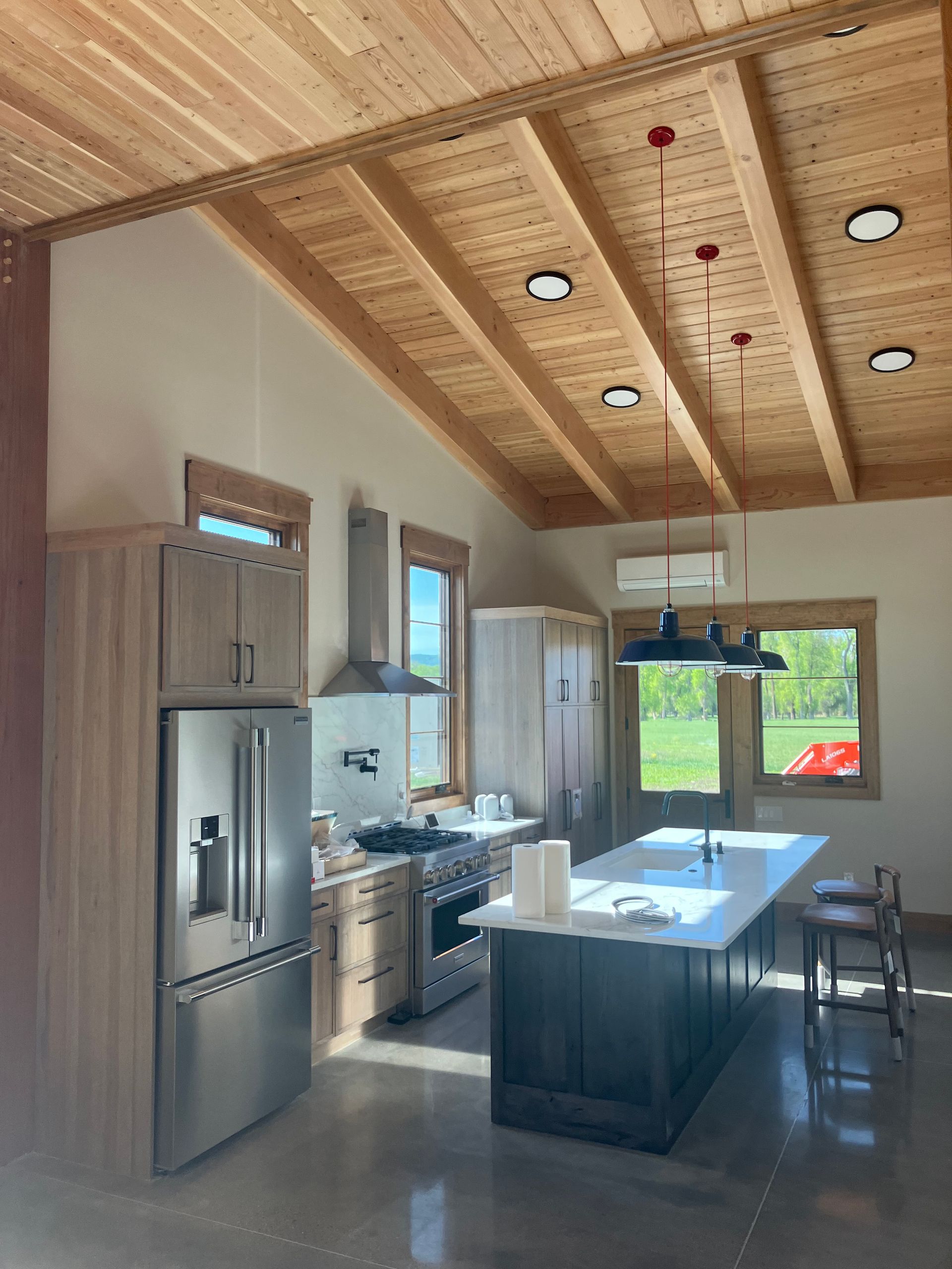 Kitchen with wood ceiling, stainless steel appliances, island, and windows overlooking a field.