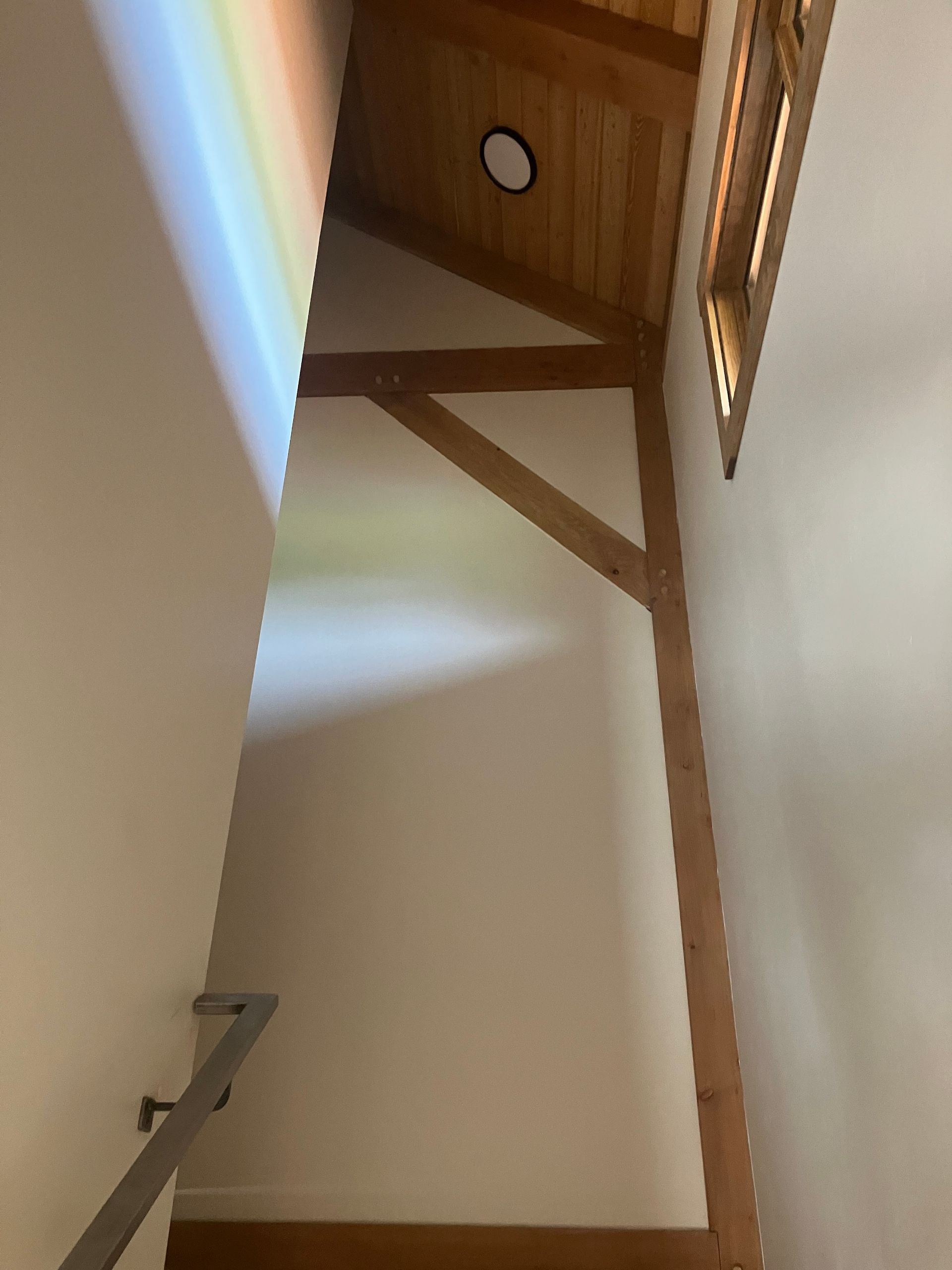 Wooden beam support in an angled ceiling, with a rainbow-like light on the wall.