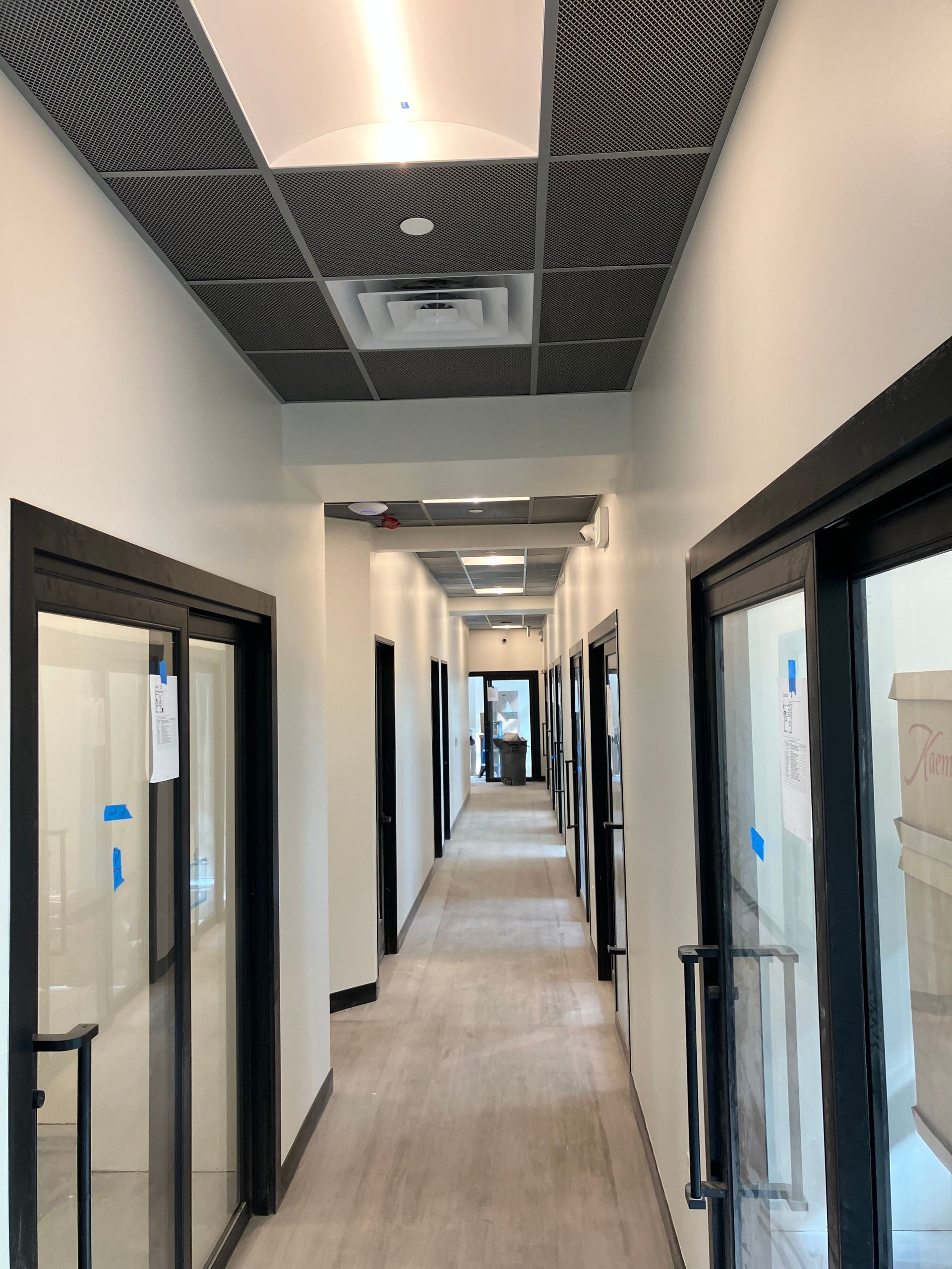 Hallway with doors, light wood-look floor, black door frames, patterned ceiling tiles.