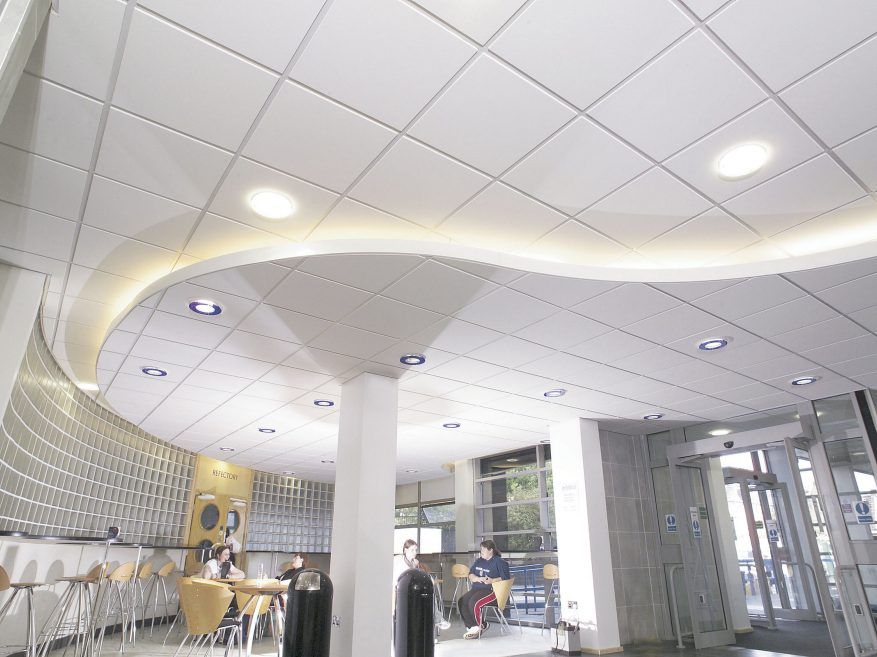 White ceiling with grid and curved section, recessed lights, cafe setting with people.
