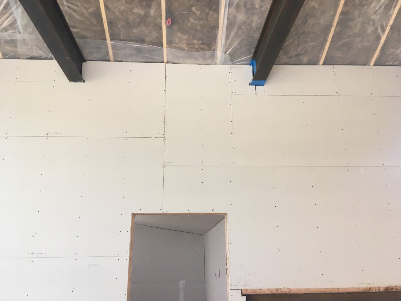 White drywall wall with a doorway cutout, metal beams overhead.