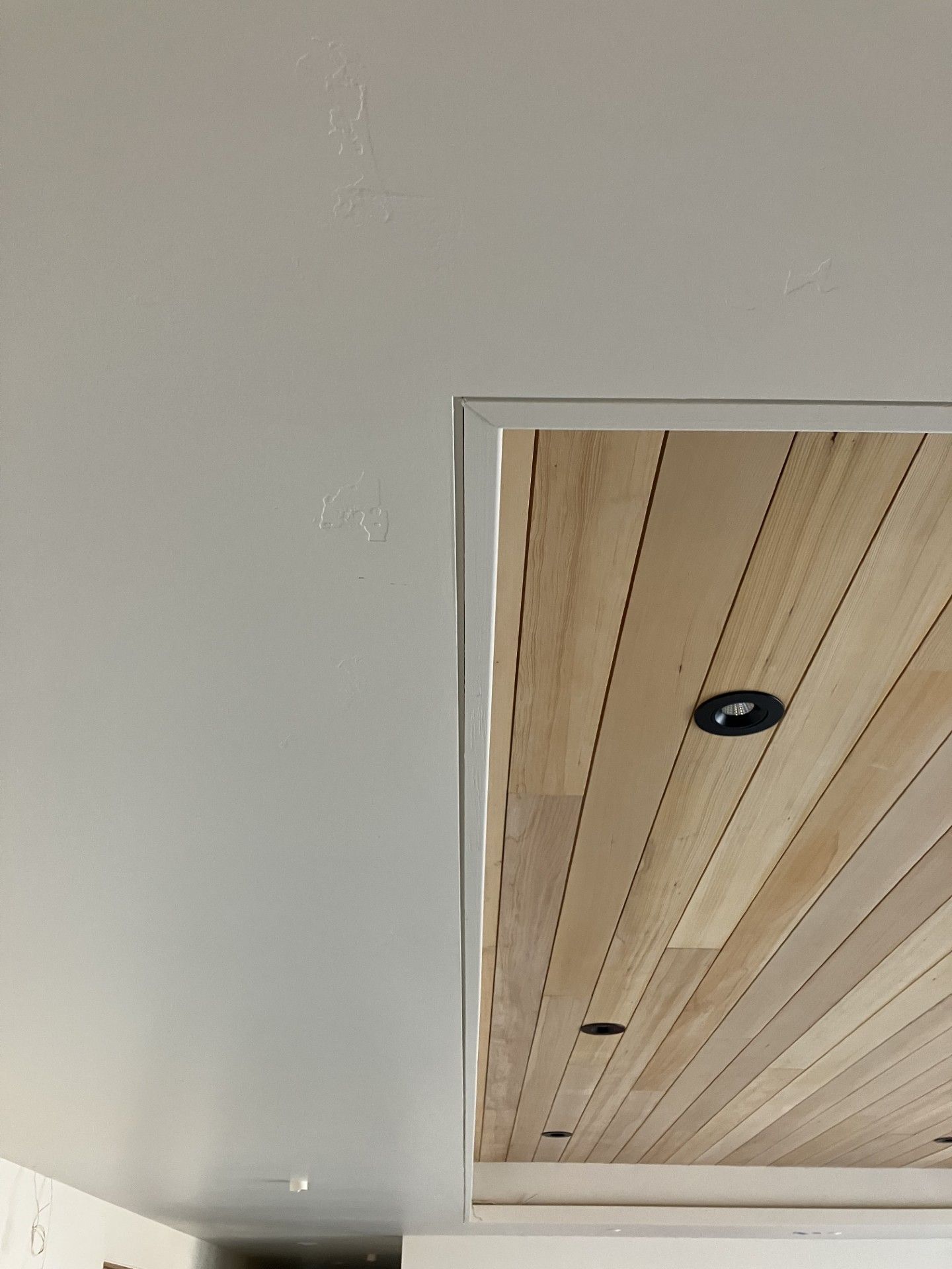 Light-colored wall and wooden ceiling with recessed lighting; a rectangular opening.
