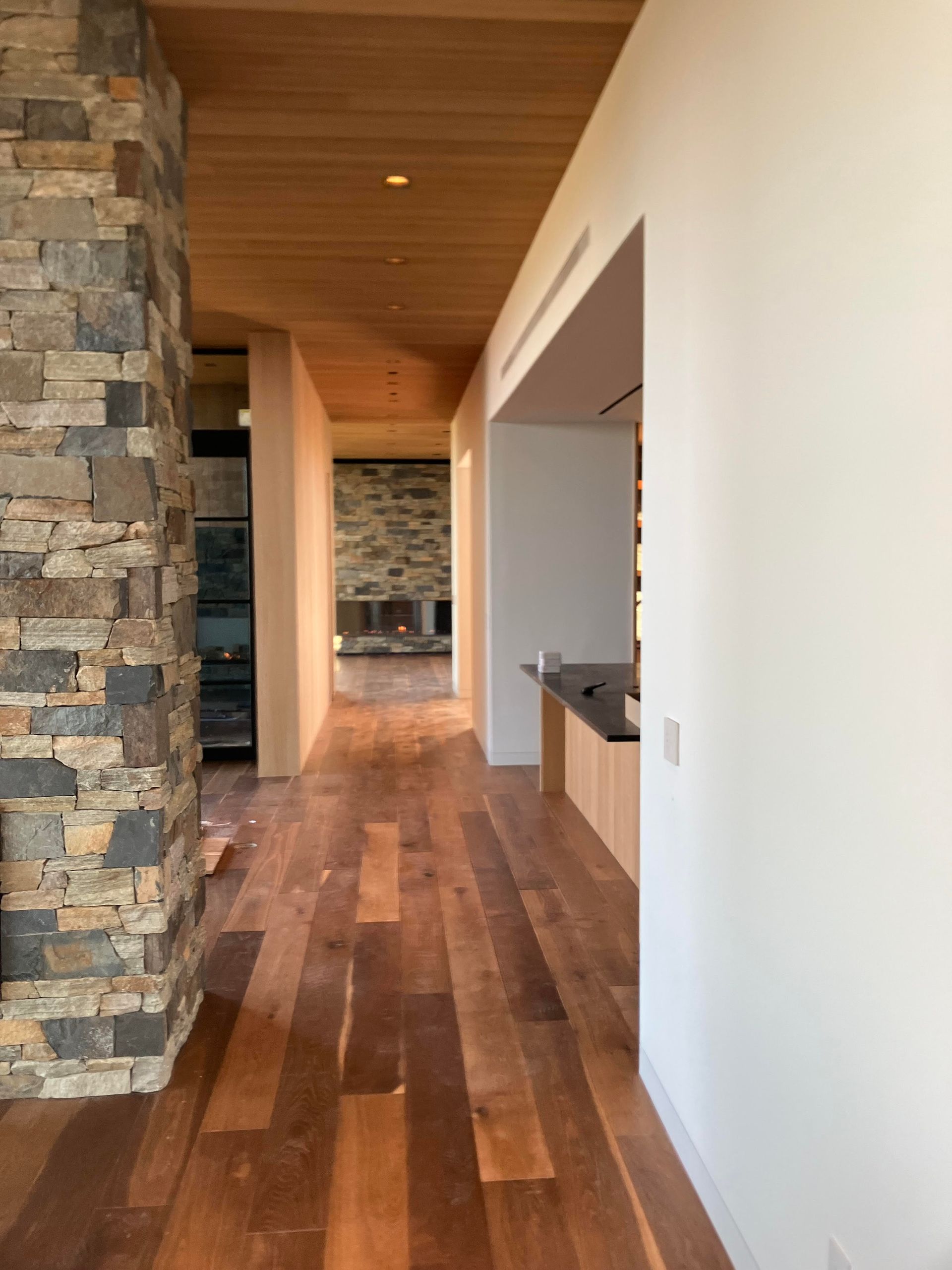 Long hallway with wood floor and ceiling, stone column, and white walls.