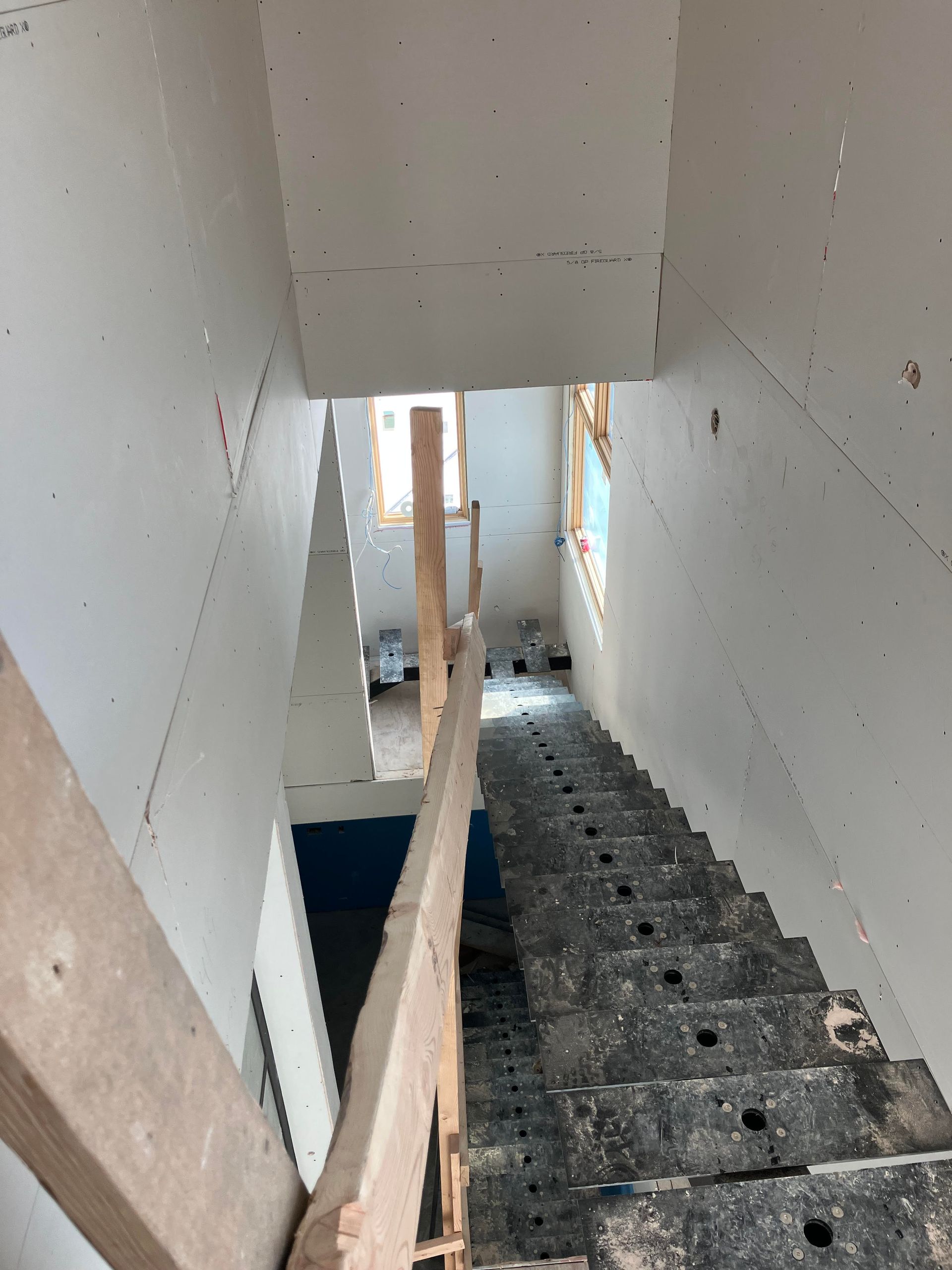 Staircase viewed from above. Concrete stairs with a wooden railing and a narrow opening at the top with windows.
