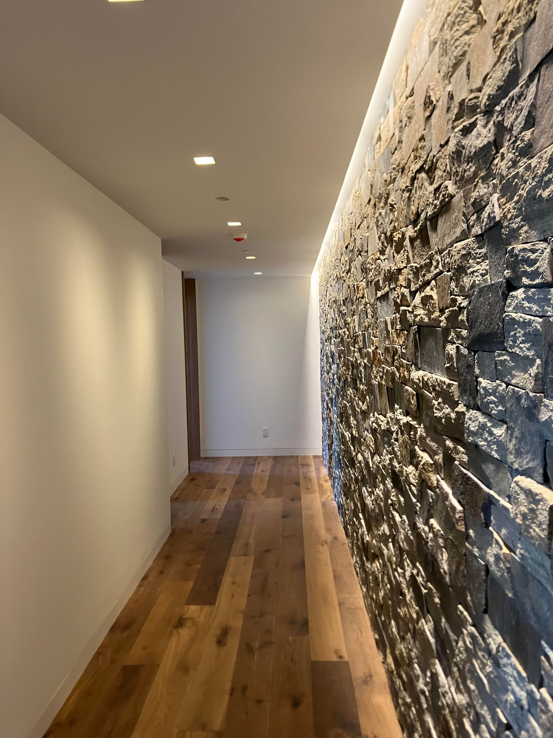 Hallway with wood floor and a textured stone wall, lit by recessed ceiling lights.