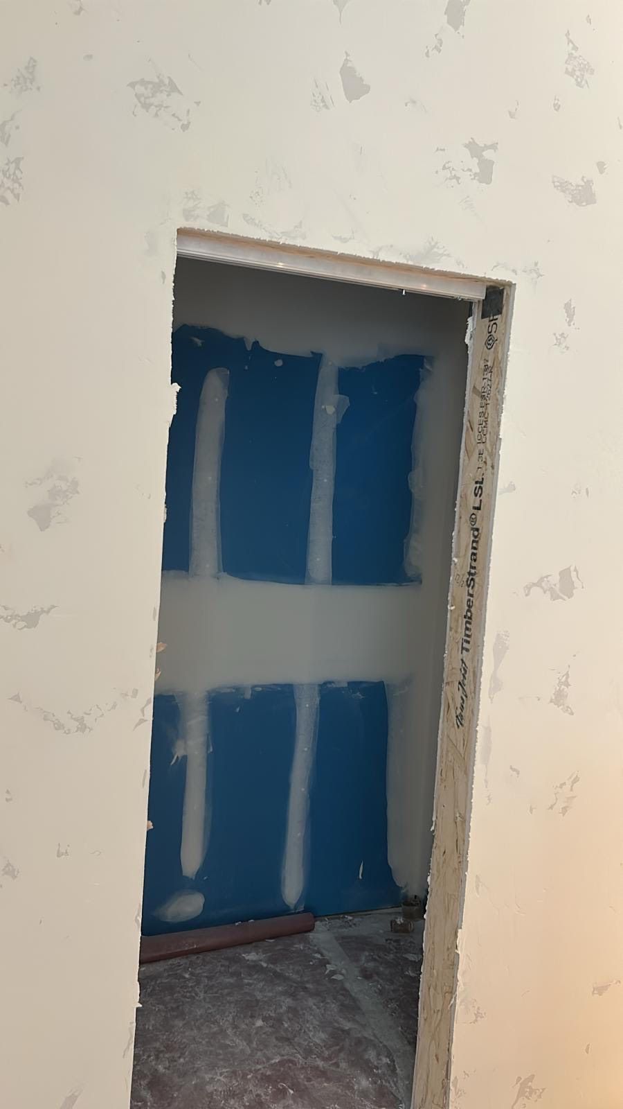 An unfinished doorway in a room. Blue drywall visible inside the opening. White walls outside.