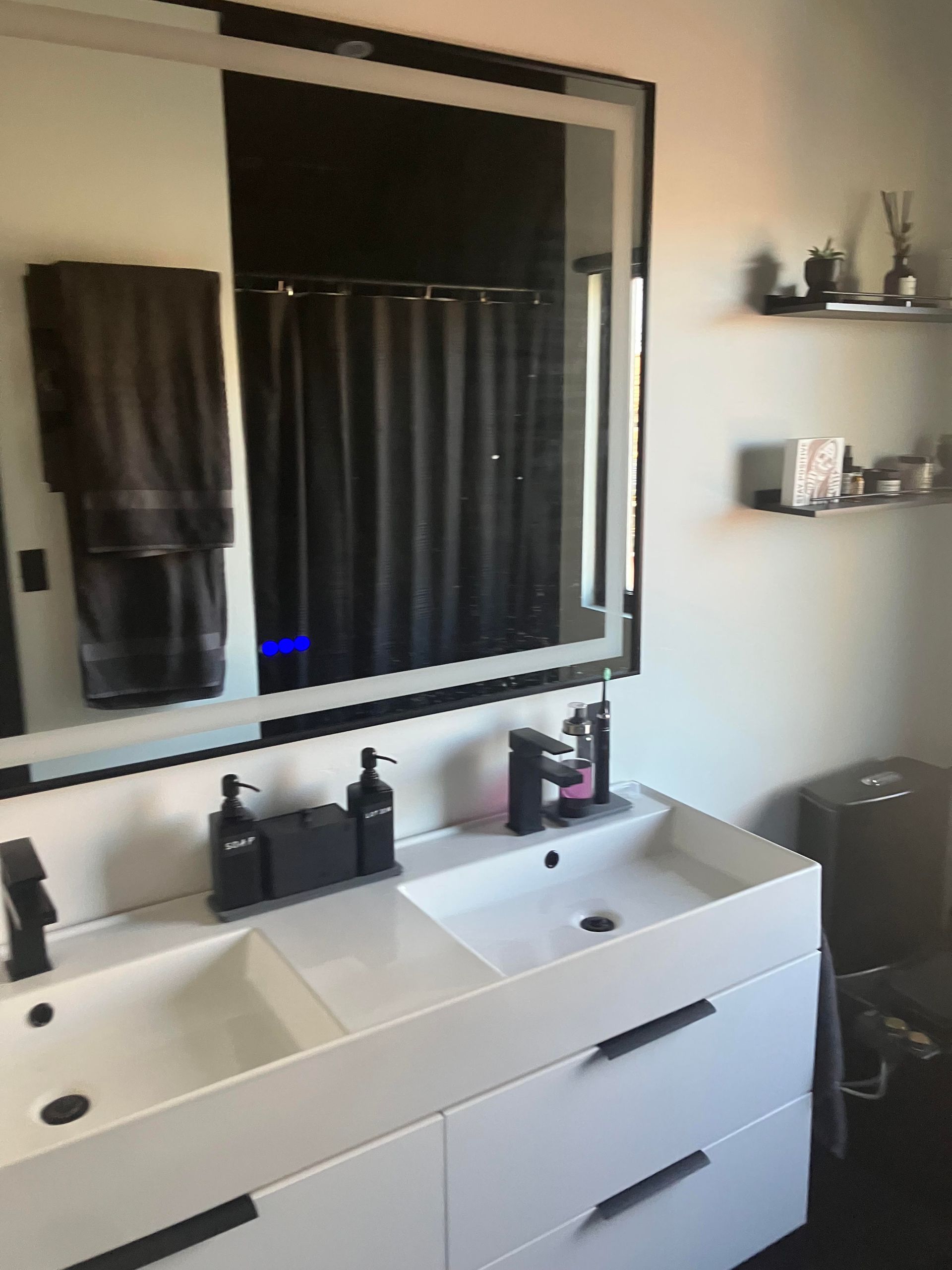 Modern bathroom with double sink, large mirror with LED lighting, and dark shower curtain.