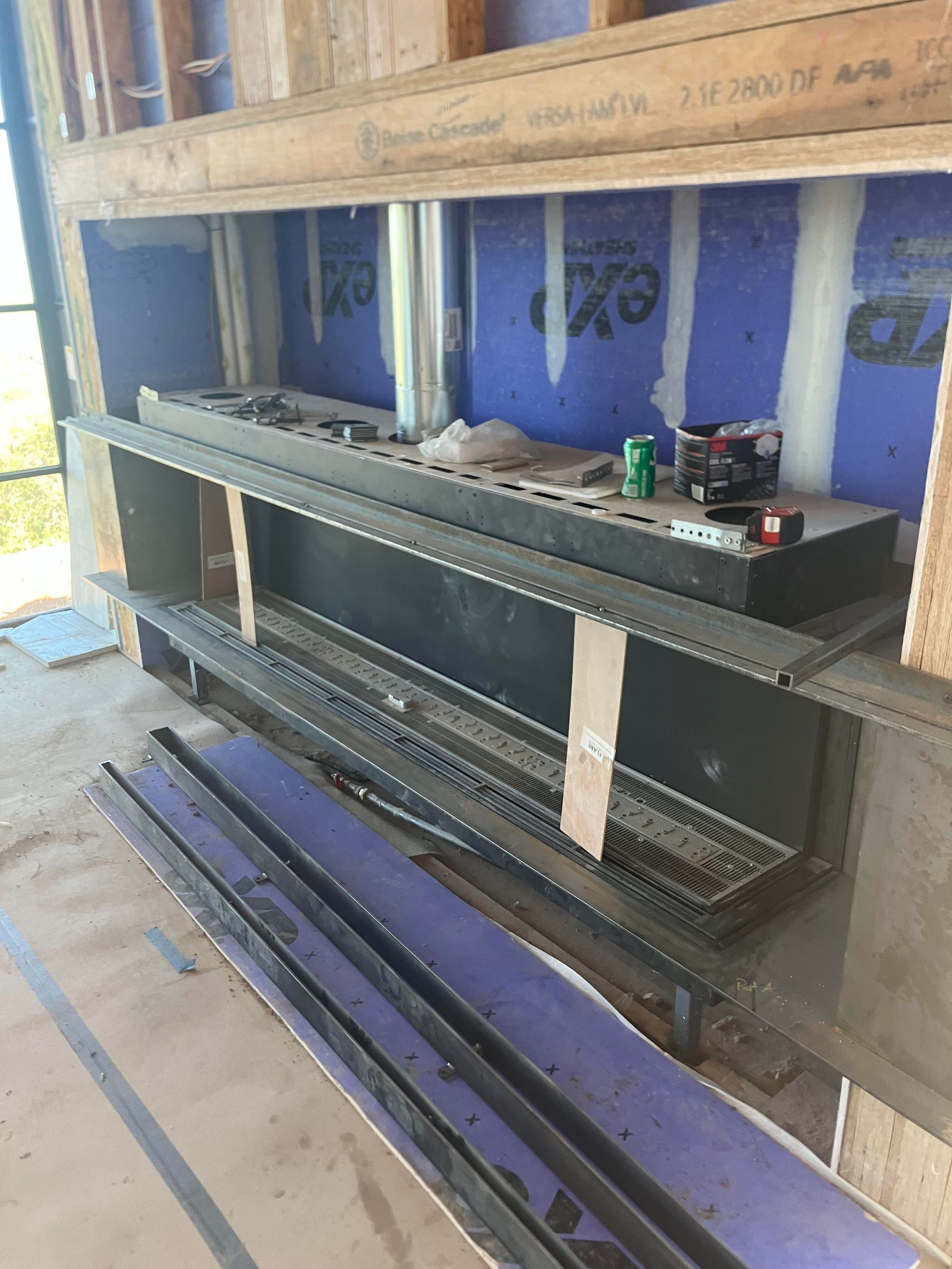 Construction site: Built-in shelving unit, black and gray steel, on blue and wood panels. Tools and debris visible.