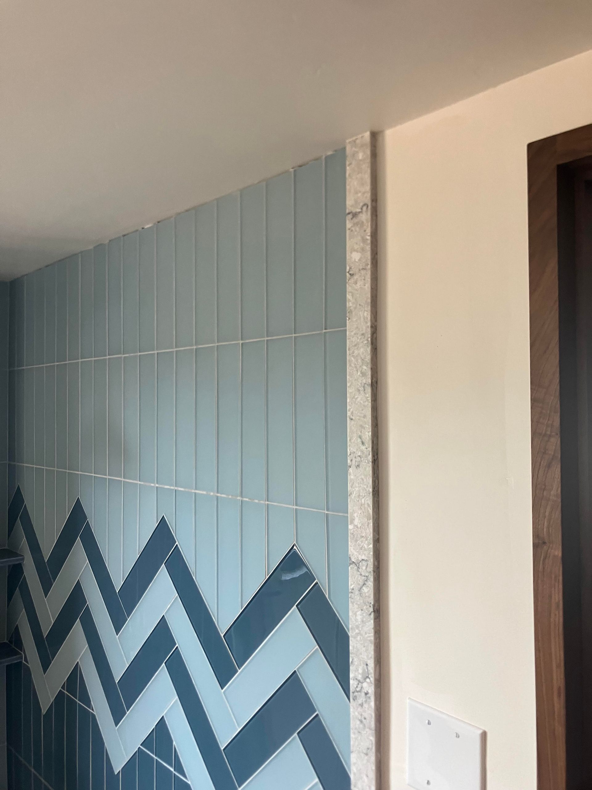 Blue tiled wall with a chevron pattern, next to a beige wall and a dark door frame.
