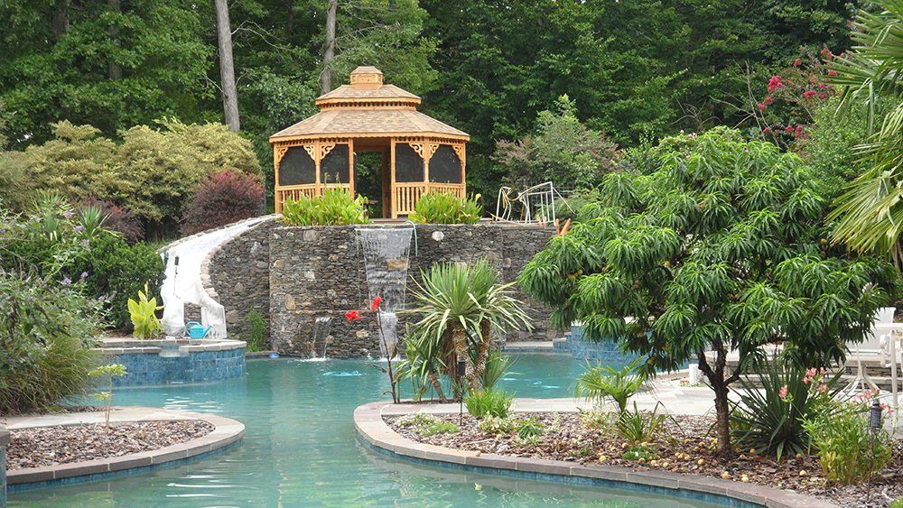 Poolside gazebo with flowing water, surrounded by lush greenery and a swimming pool.