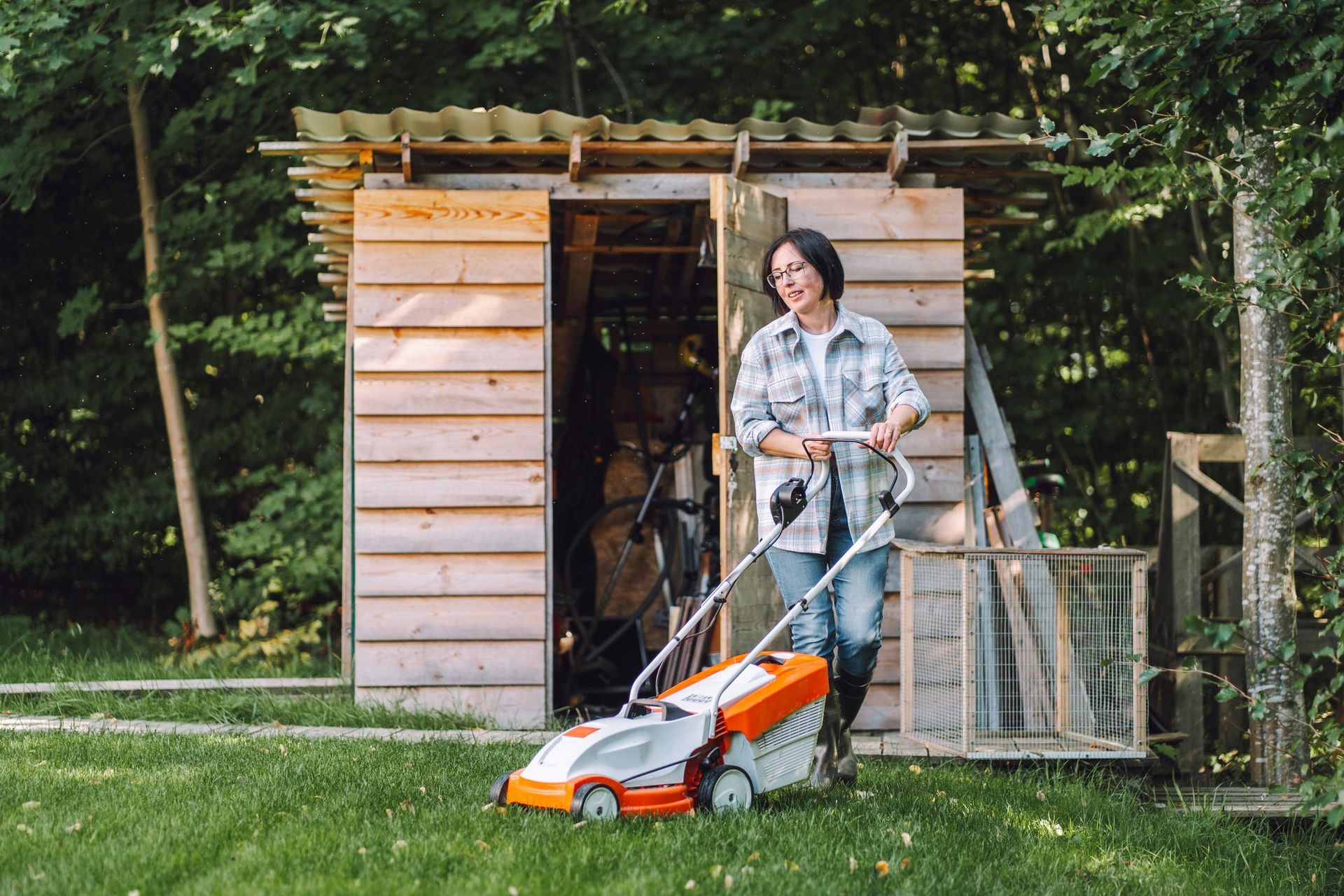 Woman bringing out lawnmower from shed in the backyard. Woman bringing out lawnmower from shed in the backyard.