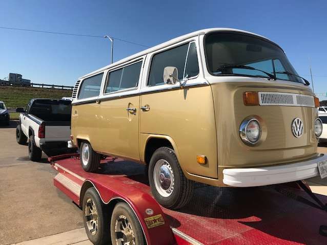 A gold and white vintage Volkswagen bus on a red trailer.