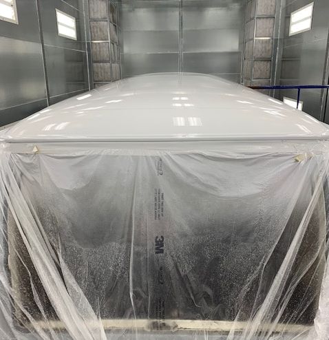 White object covered in plastic wrap inside a spray paint booth.