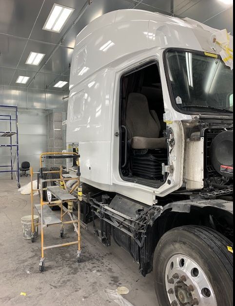 White semi-truck cab in a paint booth undergoing repair.