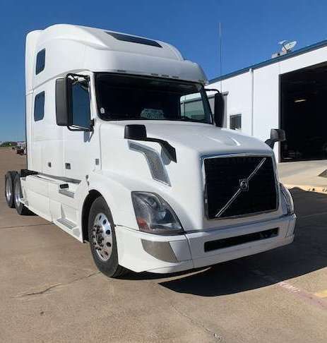 White Volvo semi-truck parked in front of a building on a sunny day.