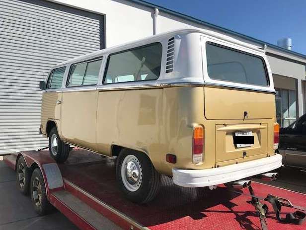 Beige and white Volkswagen bus on a red trailer, parked in front of a building.