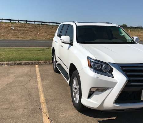 White Lexus GX SUV parked on concrete with a grassy area in the background under a blue sky.