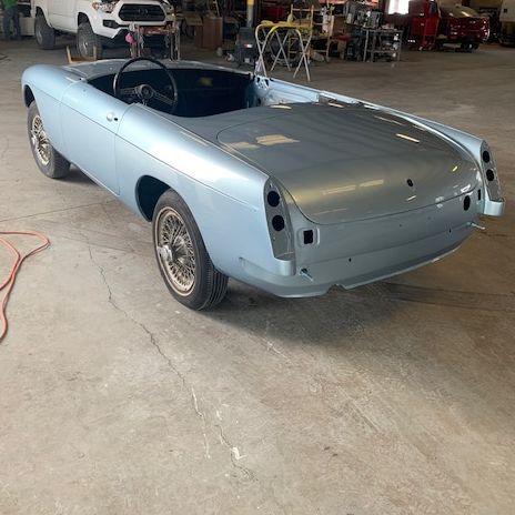 Light blue convertible car in a workshop, rear view, no doors or top, on tires.