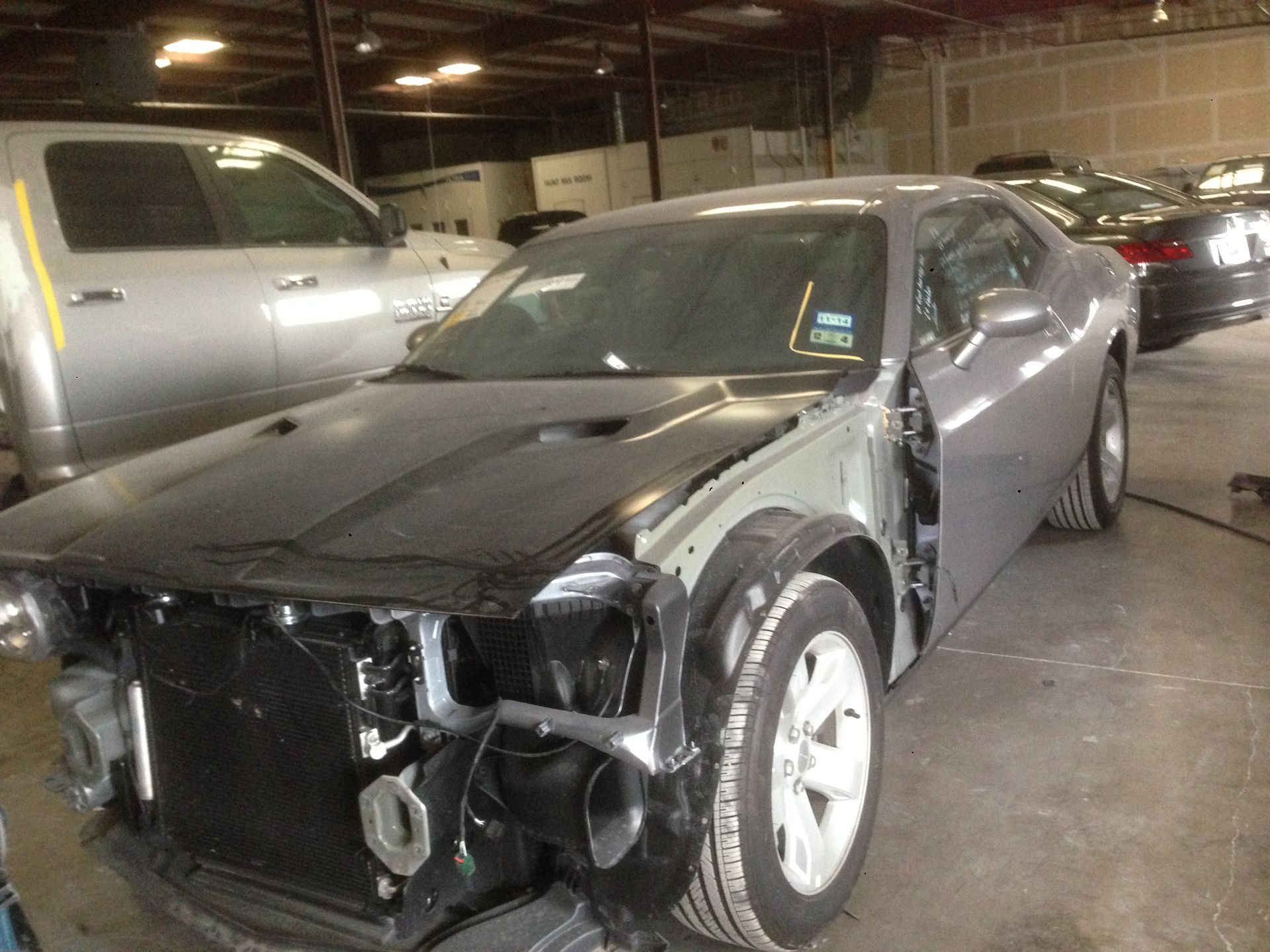 Silver car missing front end parts in a repair shop.