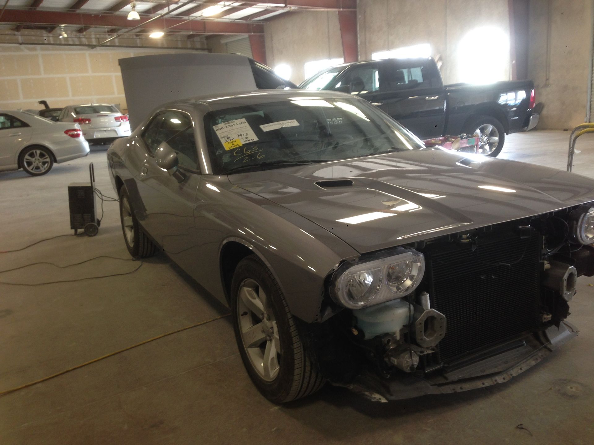 Grey Dodge Challenger undergoing repair in a shop; front bumper and hood removed, other cars in the background.