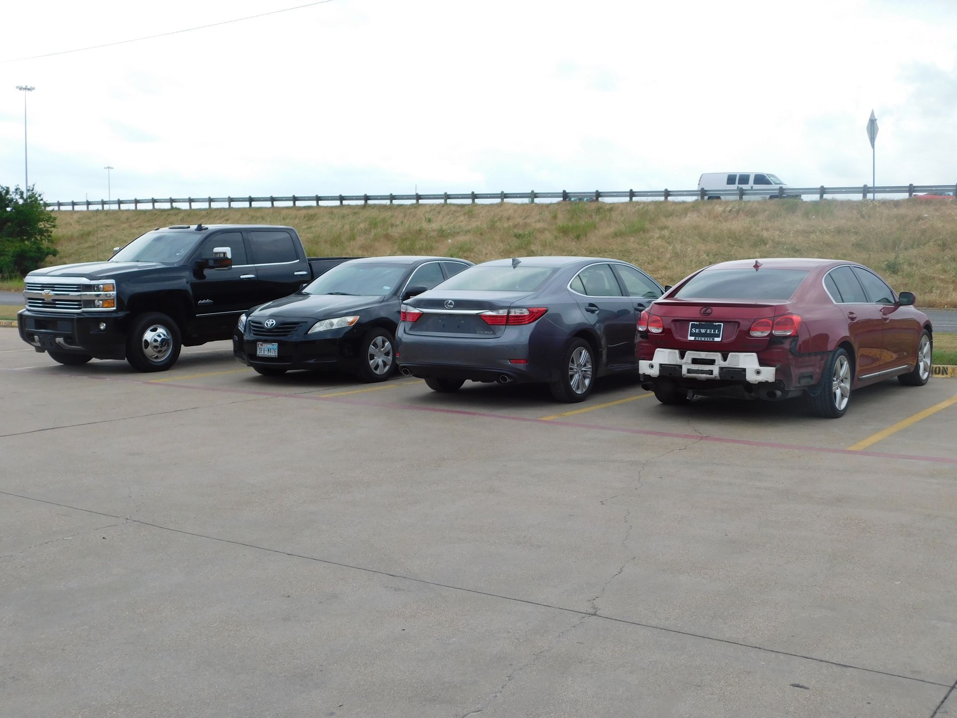 Four vehicles parked in a lot; a black truck, two sedans, and a red car. Overcast sky.