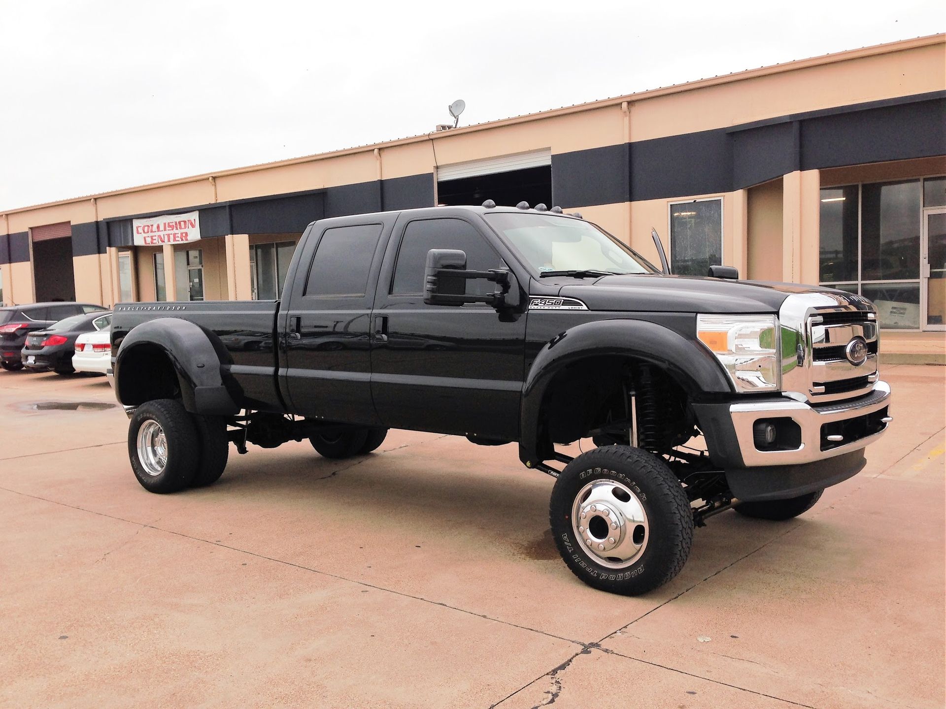 Black Ford F-350 dually pickup truck parked on pavement in front of a tan and black building.