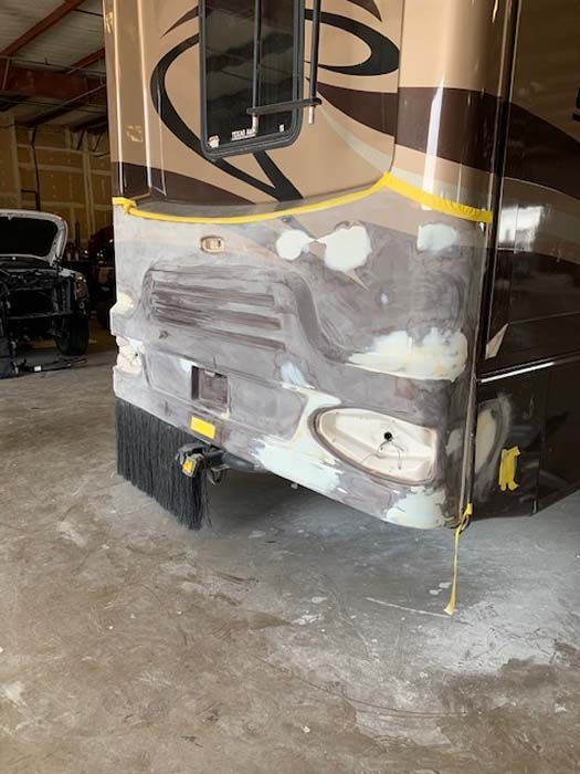 Rear of a motorhome being repaired, showing bodywork with patches and tape, in a workshop.