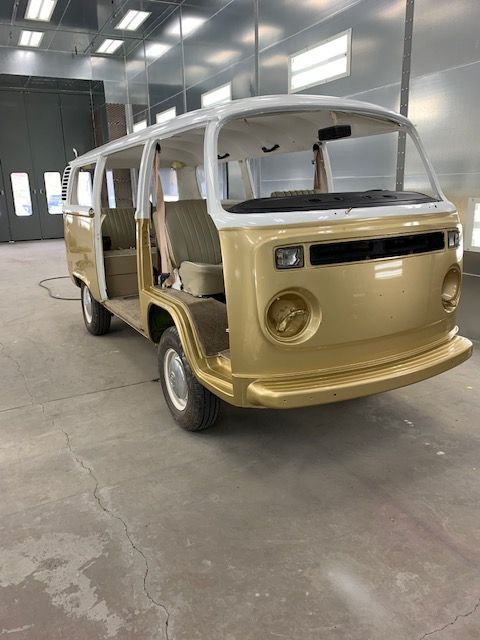 Gold and white vintage Volkswagen bus in a garage, doors open.
