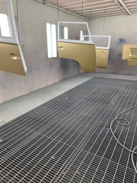 Vehicle doors and parts, painted gold, hang in a spray paint booth.