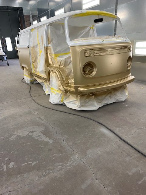 Gold painted vintage VW bus in a workshop, masked for finishing touches.