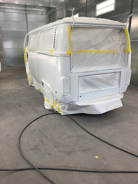 White Volkswagen van in a spray booth, partially masked with yellow tape and white paper, ready for painting.
