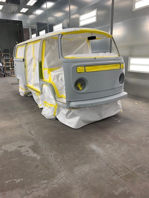 Gray Volkswagen van in a spray booth, taped and masked, ready for painting.
