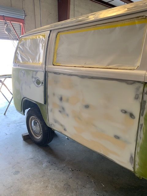Green and white vintage Volkswagen van in a workshop, undergoing body work. Masked windows and exposed primer patches.