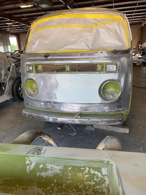 VW bus body being restored, taped for painting in a workshop. Green and silver colors.
