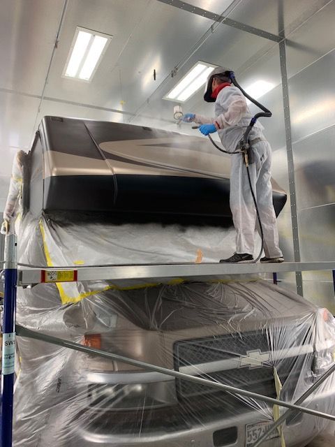 Person painting a motorhome in a spray booth, wearing protective gear.