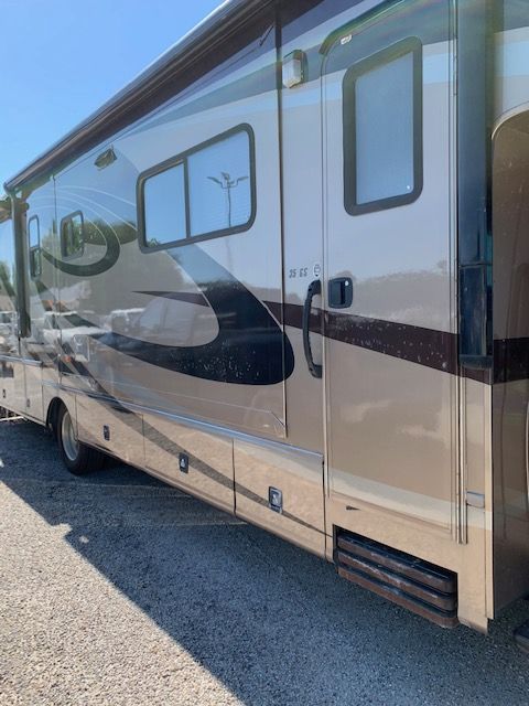 Tan and brown RV parked outside on a sunny day. The entry door is open.