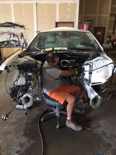 Mechanic seated in a car, working on the engine, partially disassembled. Garage setting.